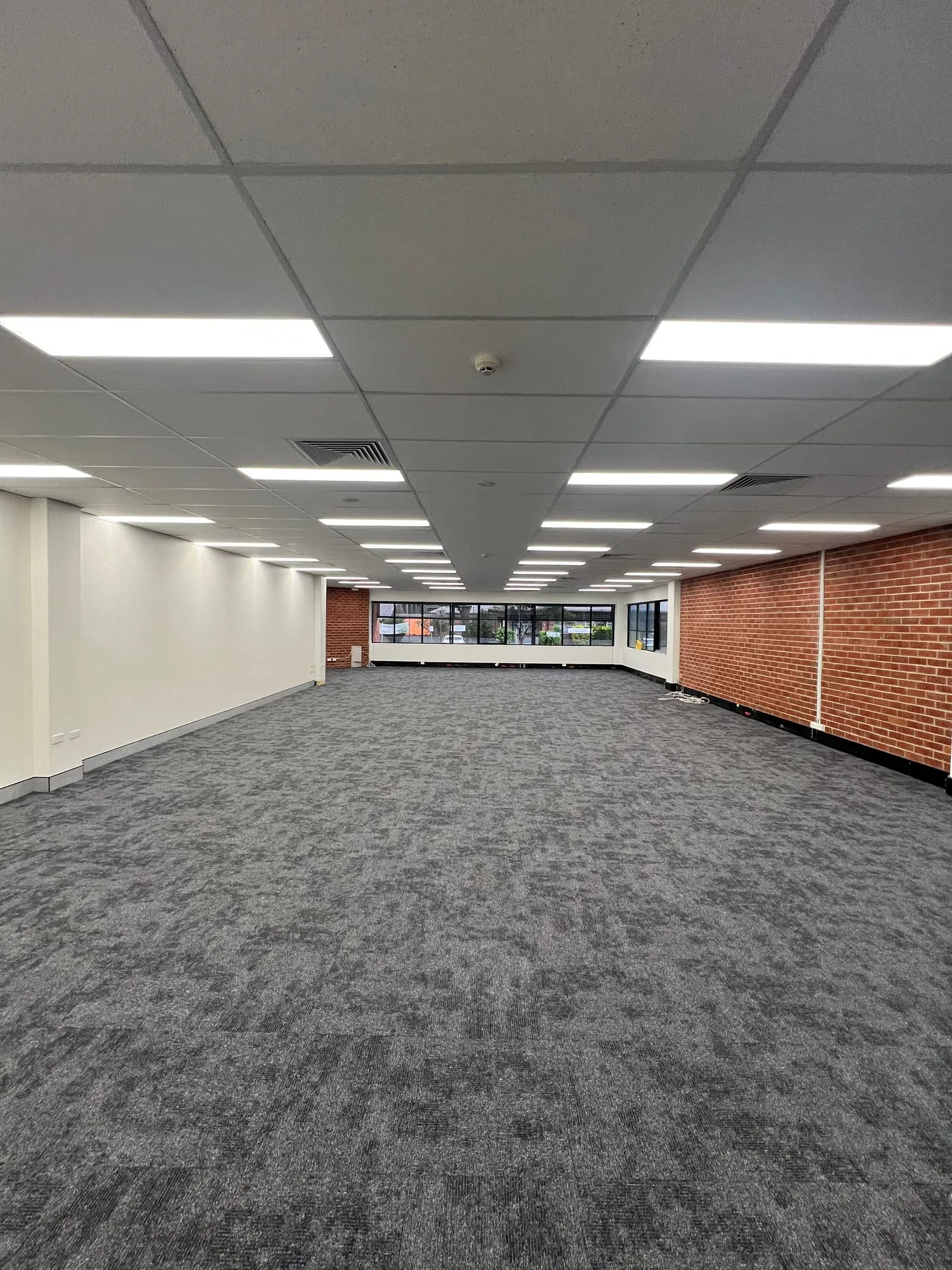 Open-plan office fit-out in Coffs Harbour with new carpet tiles and exposed brick wall