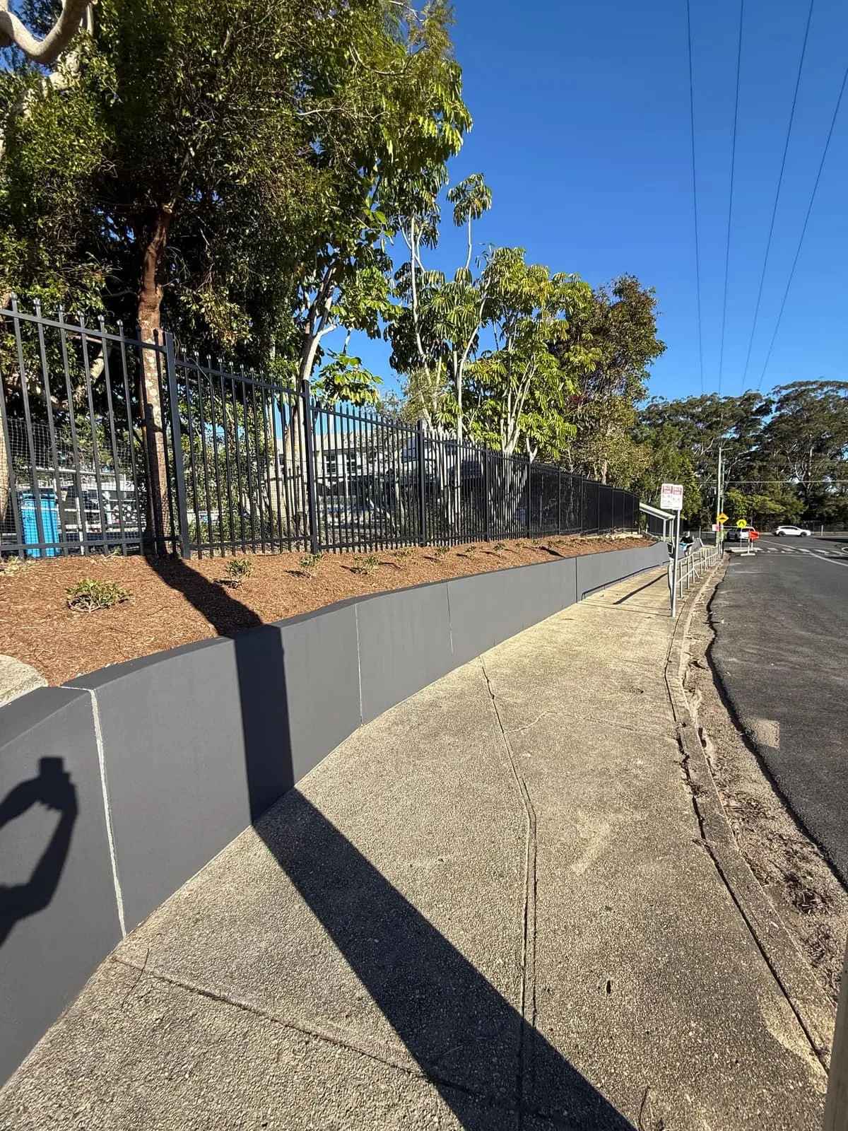 Rendered retaining wall curving along the footpath below the school palisade fence, Nambucca Heads