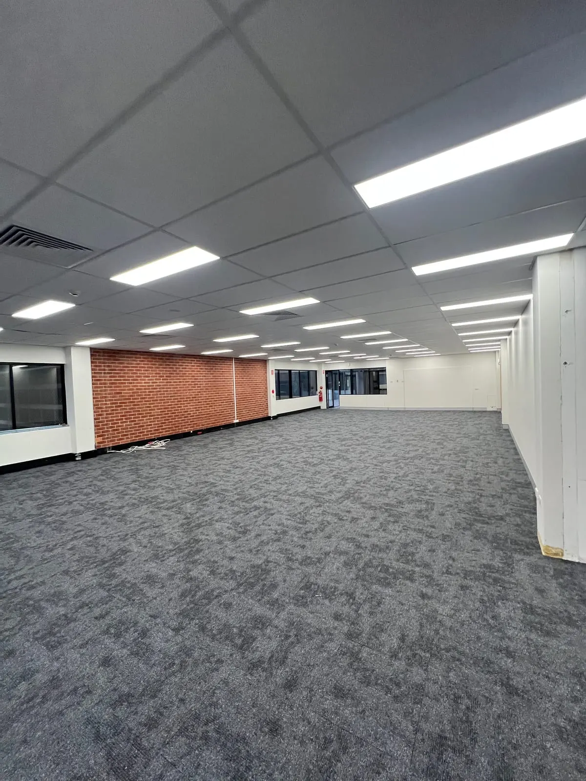 Open-plan office floor at Rigby House with new carpet tiles and exposed brick wall