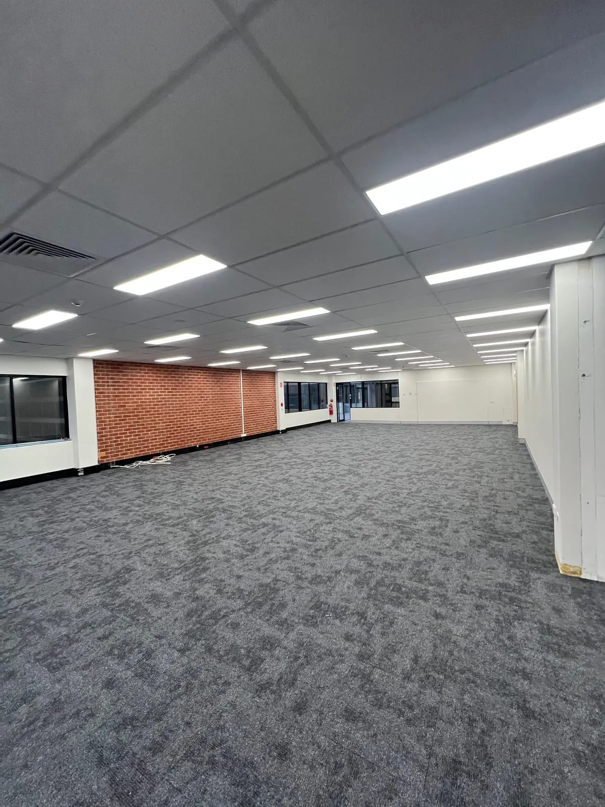 Open-plan office floor at Rigby House with new carpet tiles and exposed brick wall